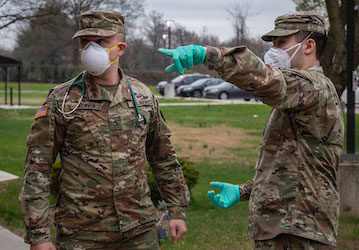 Two military members wear masks and one points during military training that requires resilience and teamwork during a crisis