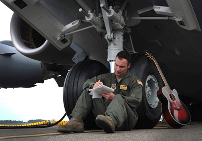 Airman writes in a journal to mentally prepare for deployment while leaning against the front tires of a military aircraft   