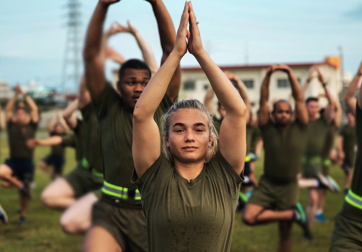 Marines practicing yoga with woman at center with hands above her head and palms together