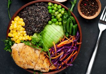 Bowl with Quinoa, chicken breast, avocado, red cabbage, arugula, carrot, green peas, corn, broccoli, green beans in a plate on a stone background,